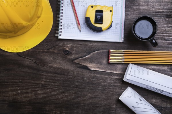 Copybook pencil blueprints instruments of measurement hard hat and coffee on pine wood board