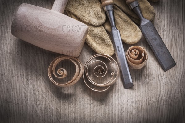 Wooden mallet curled up shavings firmer chisels leather gloves on wood board construction concept