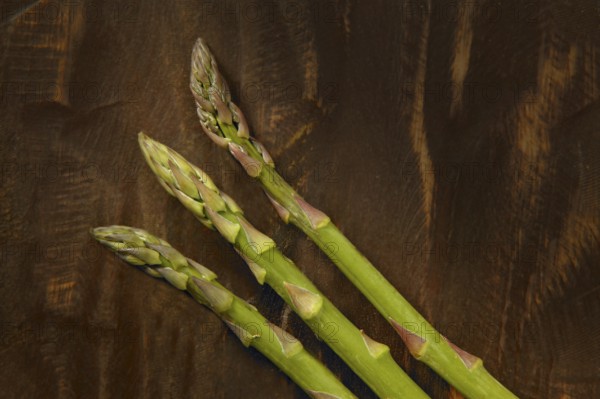 Three asparagus over dark brown wooden background