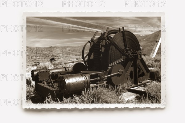 A monstrous old machine used in gold mining, rusting away in the former gold mining town of Bodie. Photo in sepia tones with white jagged edge, reclining shadow. A monstrous, old machine used in gold mining rusting in the former gold mining town of Bodie. Photo in sepia tones, all around a white jagged edge in the character of old photos