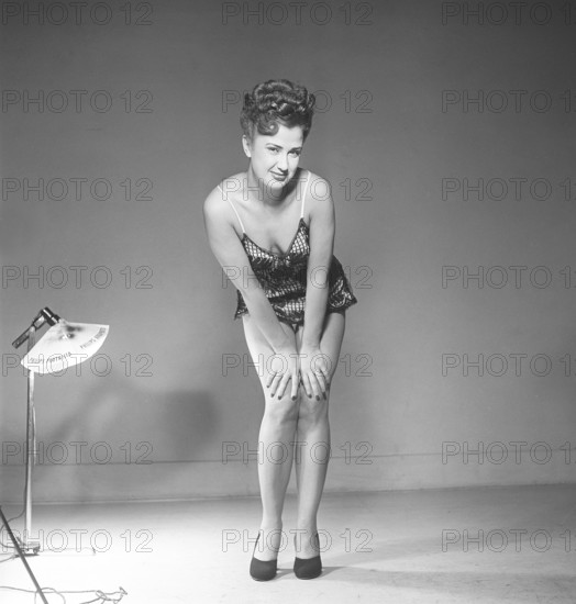 Sweden 1948. Kristoffersson Ref AT46-9 Woman in photo studio back in the day. A young woman with long slender legs, standing in a short dress poses and smiling at the camera. She has her hair done in the typical 1940s manor and on her feet she has high-heeled black shoes. Kristoffersson ref AT46-9