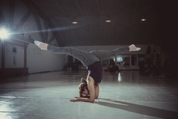 Young attractive yogi woman practicing yoga concept, standing in variation of Pincha Mayurasana exercise, handstand pose, working out, wearing sportswear, full length. handstand pose