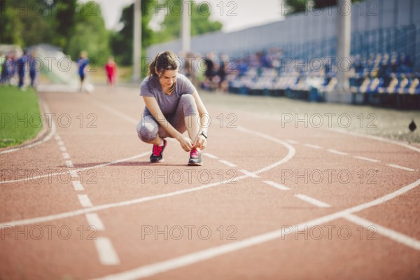 Theme sports and sportswear. A young Caucasian woman in uniform lacing shoelaces adjusting shoes sneakers on a treadmill track in a stadium