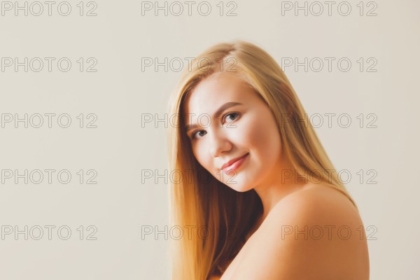 Portrait of a beautiful blonde woman with bare shoulders and back wearing natural make-up against beige background