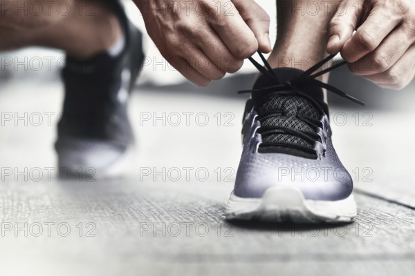 Cropped image of hands tying shoelaces on sneaker, running surface background. Hands of sportsman with pedometer tying shoelaces on sporty sneaker. Running equipment concept. Shoelaces tying by male hands