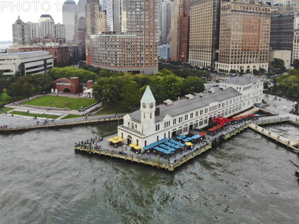 Aerial view of Battery Park pier A leading to Liberty Island, people can be seen waiting in line for boarding as well as looking at Liberty Island located opposite to the docks. October, 22nd, 2019