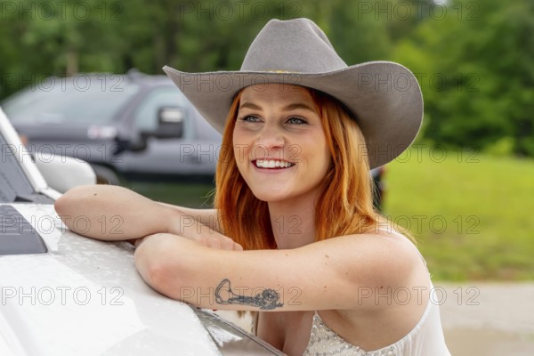 A beautiful redhead model poses in a country setting wearing cowgirl attire against her truck