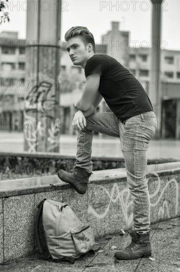 Attractive young man wearing black T-shirt and jeans with back pack standing outside