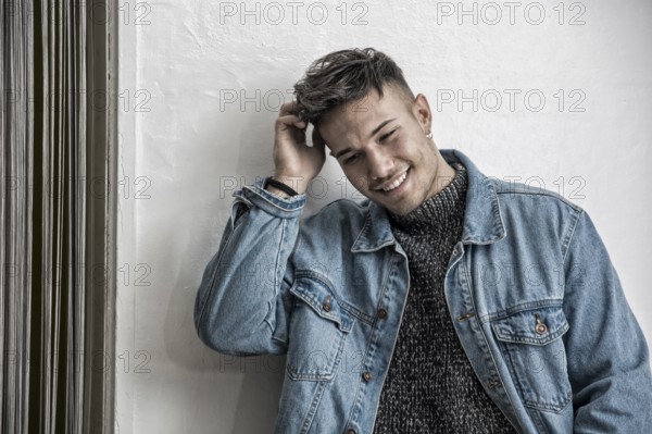 Handsome white asian young man wearing blue denim jacket, standing on light background against wall in studio shot