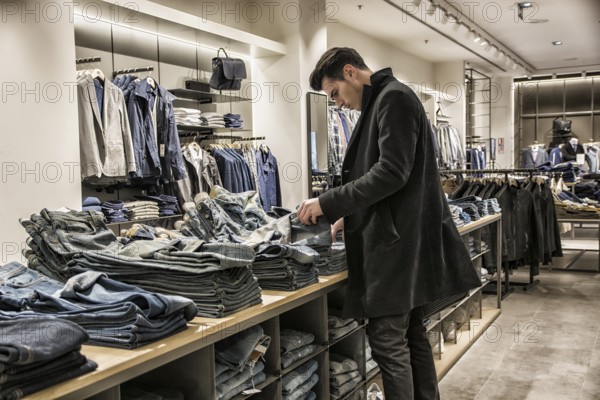 Side view of young male customer choosing shirt in menswear shop