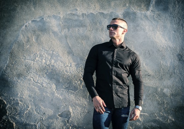 One handsome young man in urban setting in European city, standing, wearing black jacket and jeans