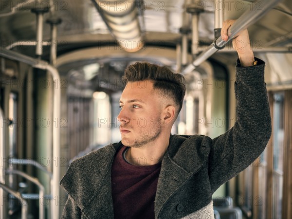 Young handsome man riding on tram or old bus in city, wearing winter clothes