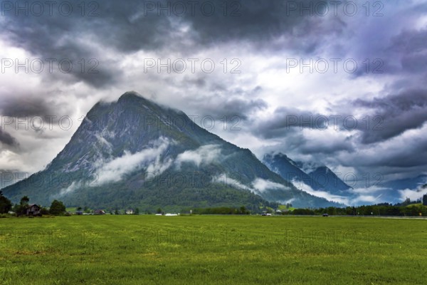 Heavy clouds covered the sky. Jostedalsbreen Park. Picturesque valley surrounded by high forested mountains. Lush green grass in the hollow. Cold summer in Norway