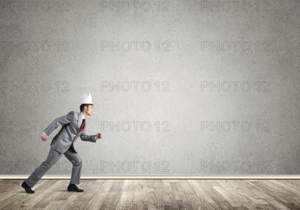 Young handsome businessman wearing white paper crown running in a hurry