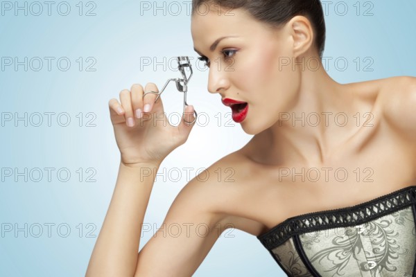 A pretty young woman holds an eyelash curler in her hand