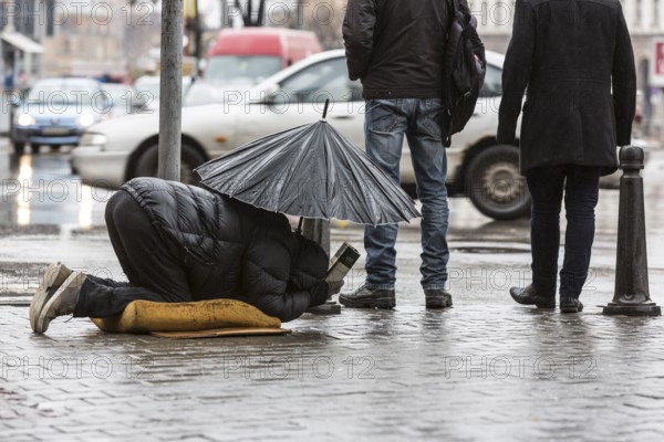 Homeless beggar is begging for money in a main street in Sofia holding an umbrella in a rainy day. Bulgaria is the poorest country in EU