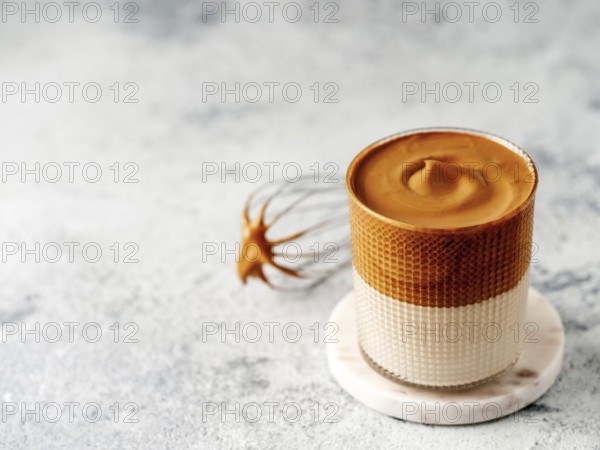 Trendy korean drink - dalgona coffee. Glass jar with cold or hot beverage - whipped instant coffee with milk and whisk on gray cement background with copy space for text or design