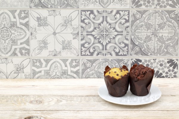 Two tempting muffins on a white plate against a vintage tile backdrop create an inviting scene to indulge