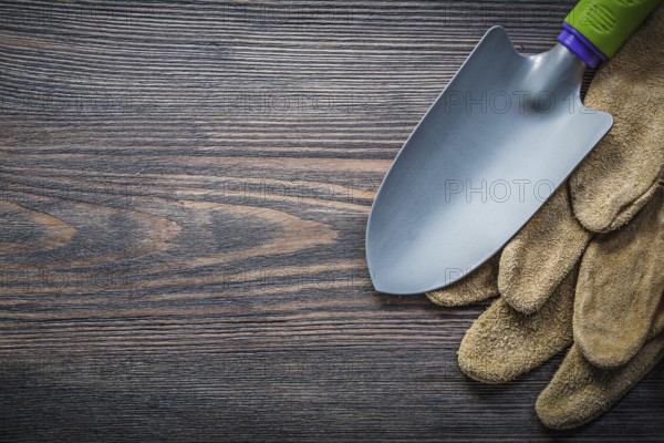 Trowel pair of leather safety gloves on wooden board directly above gardening concept