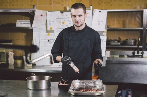 Theme cooking. A young Caucasian man in black uniform and latex gloves at a restaurant in the kitchen. Cooking mincers into a berry with a syringe. A dish of figs, fig fruit fig tree or Ficus Carian