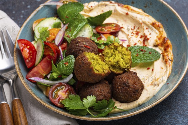 Close up of Middle Eastern Arab meal with fried falafel, hummus, vegetables salad with fresh green cilantro and mint leaves on ceramic plate on stone rustic background table. Arabic traditional cuisine, food photography
