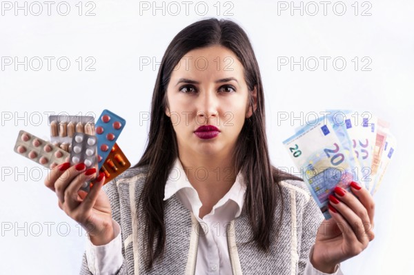 Different colorful pills and capsules in blisters and euro banknotes in the hands of angry young woman. Looking directrly in the camera. Isolated on a white background