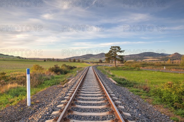 Old Railway tracks running through a field stretch to rural countryside at sunset. Single railway track at sunset, Czech Republic, Europe