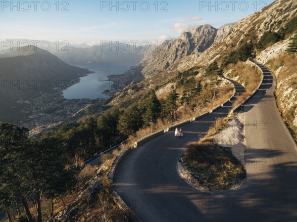 Bride and groom are walking along a high-mountain asphalt road over the bay.