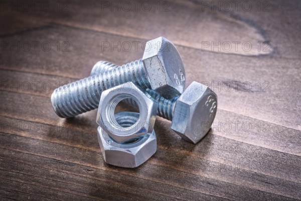 Couple of steel bolt details and screw nuts on vintage brown wooden board construction concept