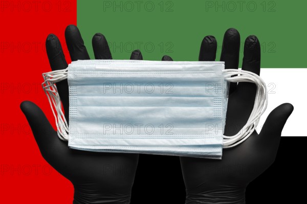 Doctor holds medical face mask in hands in black gloves on background colors national flag of United Arab Emirates UAE. Concept pandemic insurance coronavirus, quarantine, outbreak airborne diseases