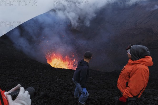 Tourists watching the beautiful volcanic eruption, standing on the slope of dangerous cinder cone of active volcano. Erupting active Tolbachik Volcano (Klyuchevskaya Group of Volcanoes) . Eurasia, Russian Far East, Kamchatka Peninsula
