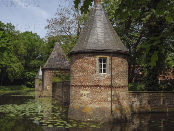 Brick building with towers reflected in a pond covered with water lilies, ochtrup, münsterland, germany