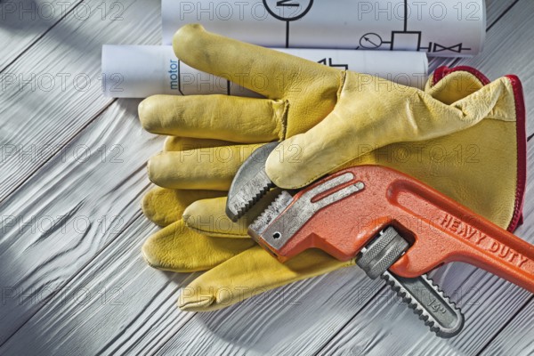 Large monkey spanner in yellow leather glove and rolled blueprints on white wood