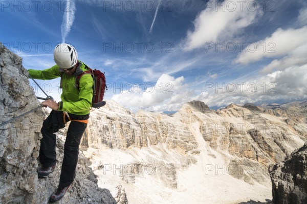 handsome male climber on a steep and exposed rock face climbs a Via Ferrata in Alta Badia in the South Tyrol