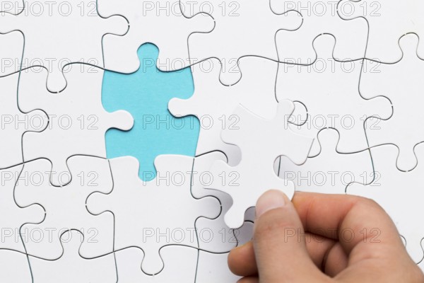 Human hand inserting white puzzle empty space