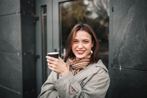 A woman in a coat and scarf laughing joyfully with a cup in hand