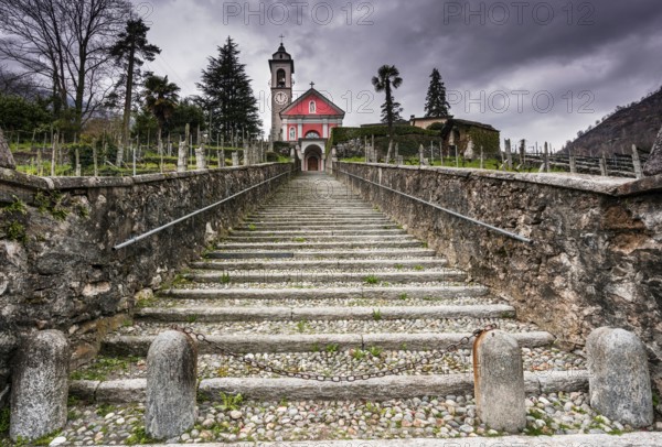 long stairs leading up to an old rose colored church under an expressive overcast sky in the Maggia Valley in Switzerland