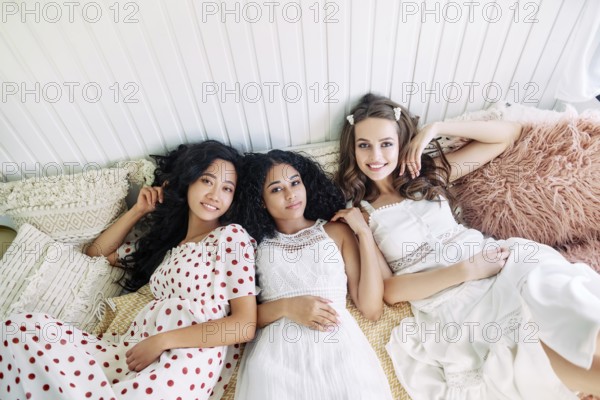 Beautiful multi ethnic girls have fun together, relax and lying on bed inside the camper van. Women friendship and females beauty concept. Caucasian, african american and asian girls posing at light interior