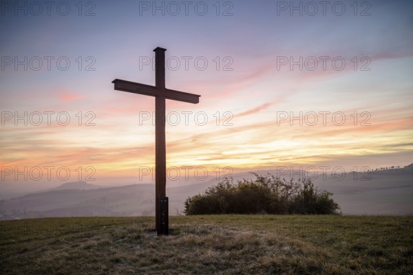 A cross stands in front of a colourful sunset in a peaceful landscape, Bisberg, Watterdingen, Hegau, Lake Constance region, Baden-Württemberg, Germany, Europe