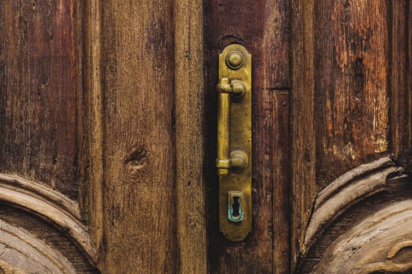 Vintage background. Brass-made old handle with Elements of an carved wooden door decorated with massive wooden simulating weaving. An old concept of old antiques. Varnished old mahogany