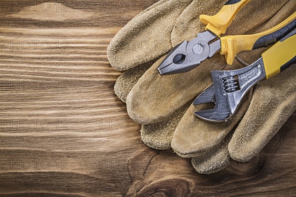 Protective gloves adjustable spanner pliers on wooden board construction concept