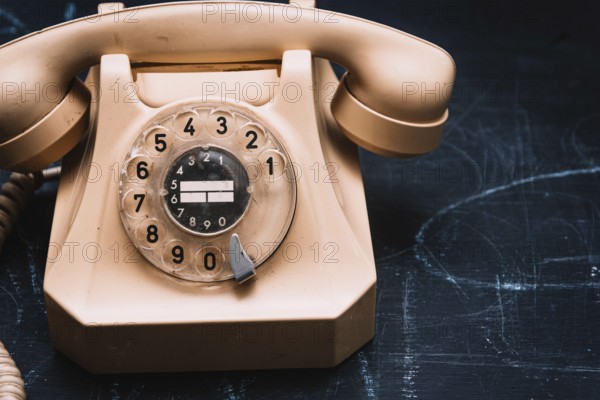 Close-up of a beige vintage rotary phone on a dark surface, evoking a sense of nostalgia
