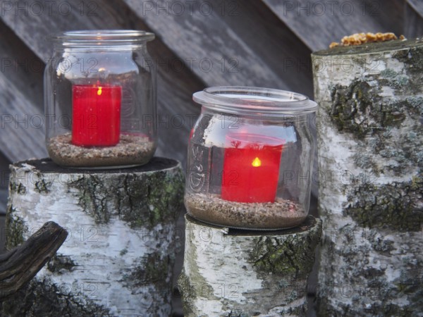 Red candles in glass jars on tree stumps against a rustic backdrop, borken, münsterland, germany