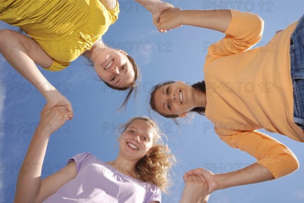Group of three friends smiling with heads together looking at camera. Low angle view