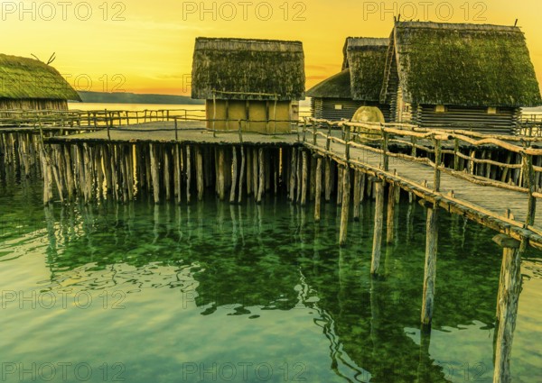 Fishing huts made from wood, clay and thatched roof, suspended on stilts over a lake water, with the beautiful yellow sunset in the background