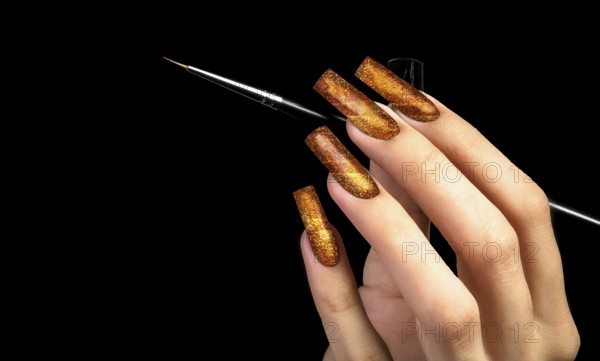 Hand with a beautiful golden manicure and a brush on a black background. Nail design. Extended nails