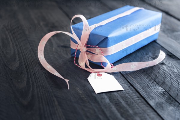 Classy blue gift, tied with pink ribbon and bow, with an empty label tied to it, on an old wooden table