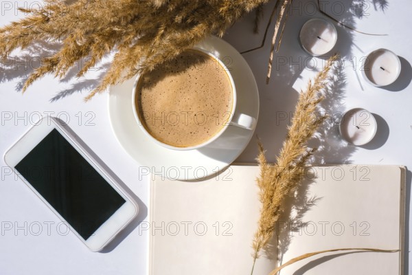 Pampas grass and white cup with coffee. Mobile phone with black screen. Checking social media Drinking Cappuccino in the breakfast morning at home. Flat lay. Wallpaper. Aesthetics Cozy home workplace