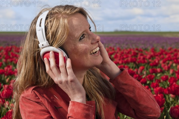 Portrait of a beautiful blond Dutch girl listening to music in tulips field