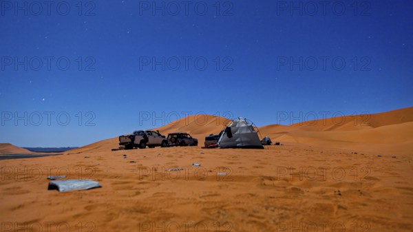 Camping scene in the desert under a starry night sky with tents and vehicles, tent camp in the dunes of the Sahara in Algeria